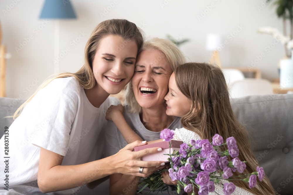 Daughter granddaughter and grandmother with gift box and flowers indoors Daughter granddaughter and grandmother with gift box and flowers indoors