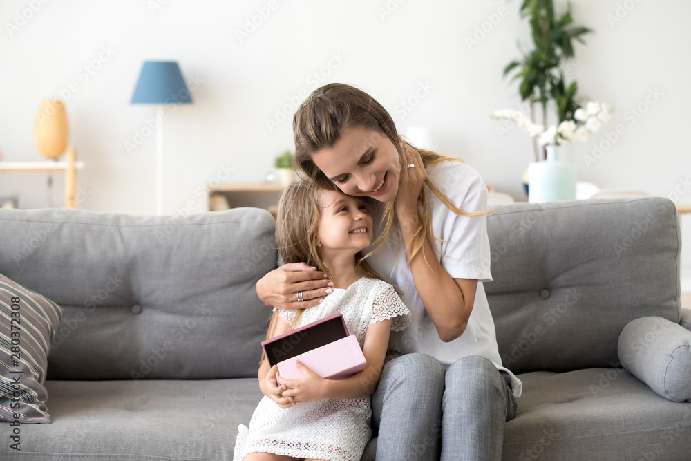 Loving mother hugging little daughter sitting together on sofa - obrazy, fototapety, plakaty 