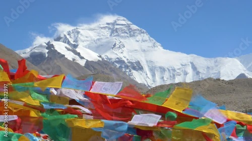 SLOW MOTION, CLOSE UP: Detailed shot of colorful prayer flags flapping in the wind blowing across the rocky foothills of Everest. Snow capped Mount Everest towers above the barren landscape in Tibet. photo