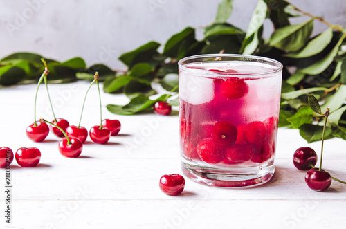 Red cocktail with cherry and ice on a white wooden background. Fresh summer cocktail with cherries and ice cubes.