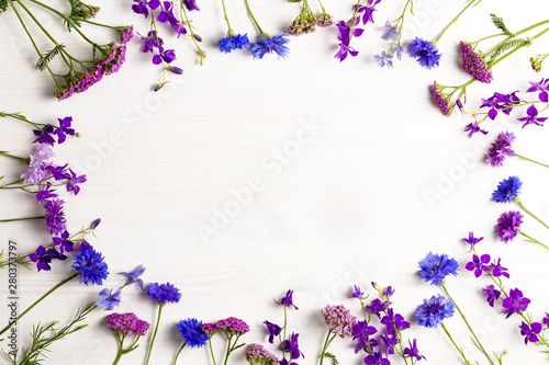 Beautiful blue and purple flowers frame flat lay on white wooden desk  copy space  top view