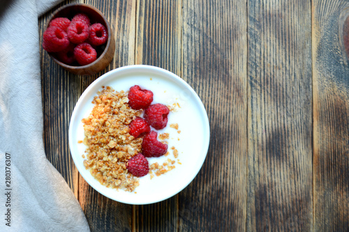 Delicious yogurt with granola and fresh raspberry in a bowl on a wooden background Healthy food concept Top view