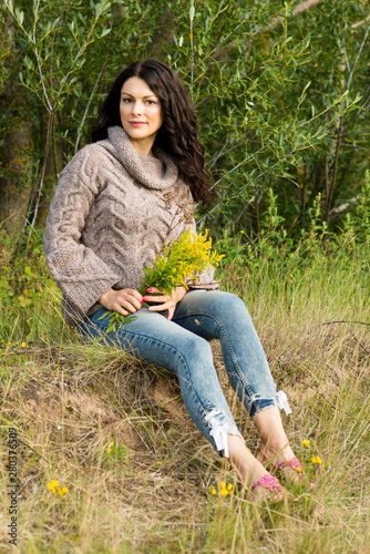 The woman in a knitted pullover poses against the background of the nature