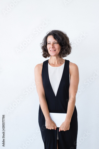 Pensive woman with tablet standing over white studio background. Positive middle aged woman holding mobile computer and looking into distance. Mobile technology concept