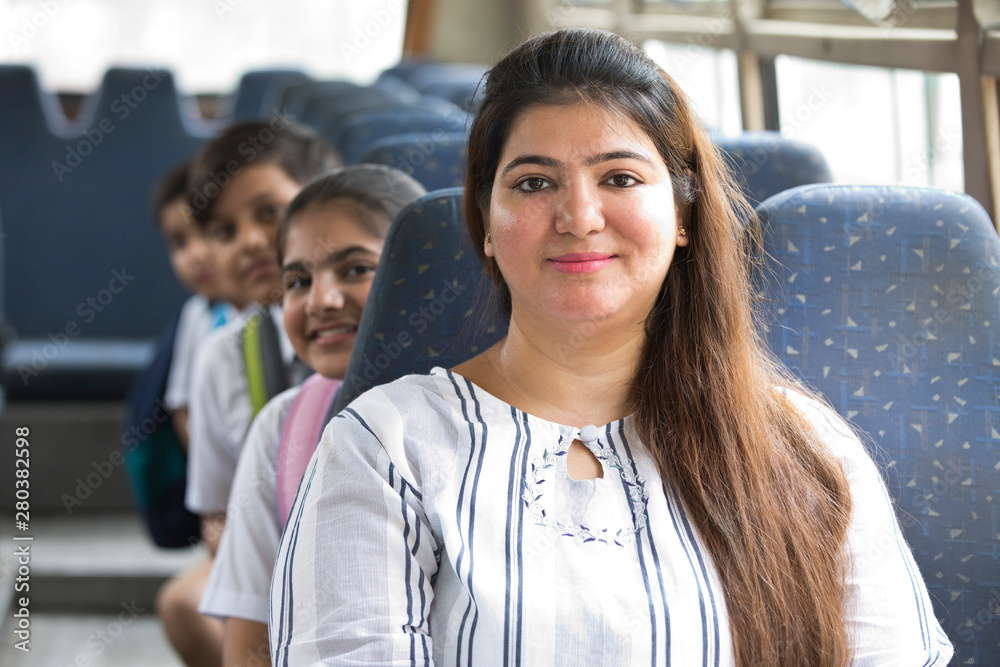 Fototapeta premium Happy teacher taking care of schoolgirl while traveling in school bus