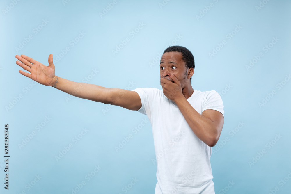Half-length close up portrait of young african-american man in white shirt on blue background. Human emotions, facial expression, ad, sales concept. Pointing, choosing, astonished. Copyspace. Half-length close up portrait of young african-american man in white shirt on blue background. Human emotions, facial expression, ad, sales concept. Pointing, choosing, astonished. Copyspace.
