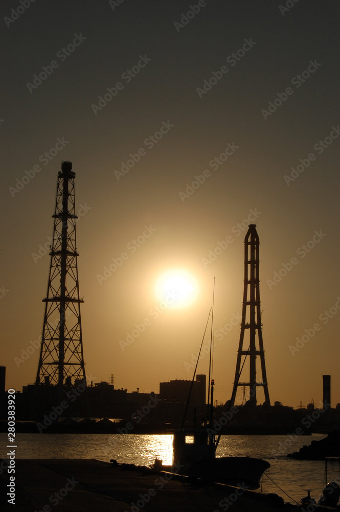 夕日でシルエットになる火力発電用の鉄塔のある港