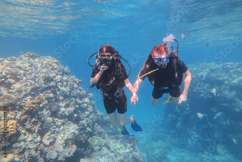 Man in snorkeling mask and suit dive underwater with tropical fishes in coral reef sea pool. Couple is swiming under the sea water. Travel lifestyle, water sport outdoor adventure concept.