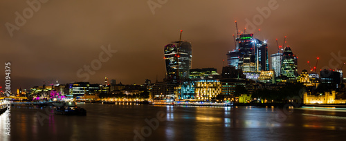 Skyline of London with its famous skyscrapers and in the foreground the Thames at night