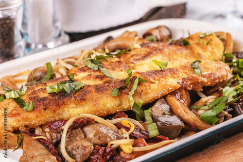 Seafood, Mediterranean cuisine. Grilled fish steak with mushrooms, oyster mushrooms, boletus, greens and onion rings. Caucasian kitchen