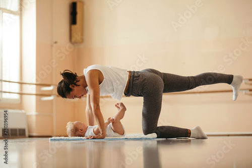 Fototapeta Naklejka Na Ścianę i Meble -  Athletic mother with baby doing stretching exercises in health club.