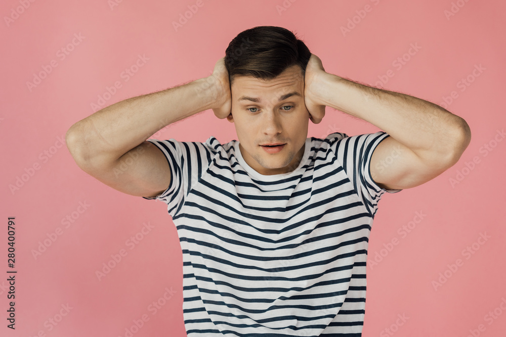 front view of young man in striped t-shirt covering ears isolated on pink front view of young man in striped t-shirt covering ears isolated on pink
