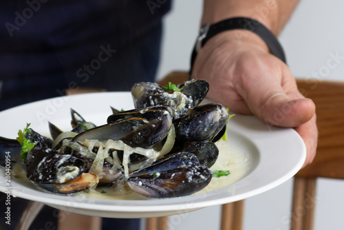 Cooked mussels in wine and cream with greens and onion served on white plate