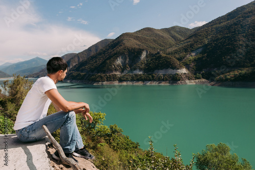 young man traveler sits and looks at a beautiful view of the Zhinvalskoe Reservoir, Georgia.