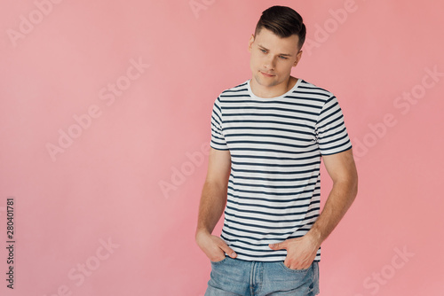 pensive man in striped t-shirt standing with hands in pockets isolated on pink