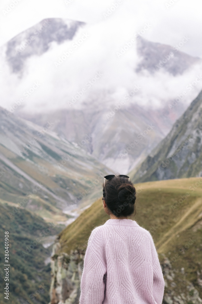 young girl in a sweater is looking at the Caucasian mountains, Georgia, rear view.