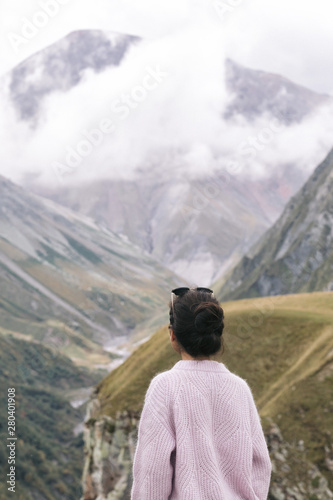 young girl in a sweater is looking at the Caucasian mountains  Georgia  rear view.