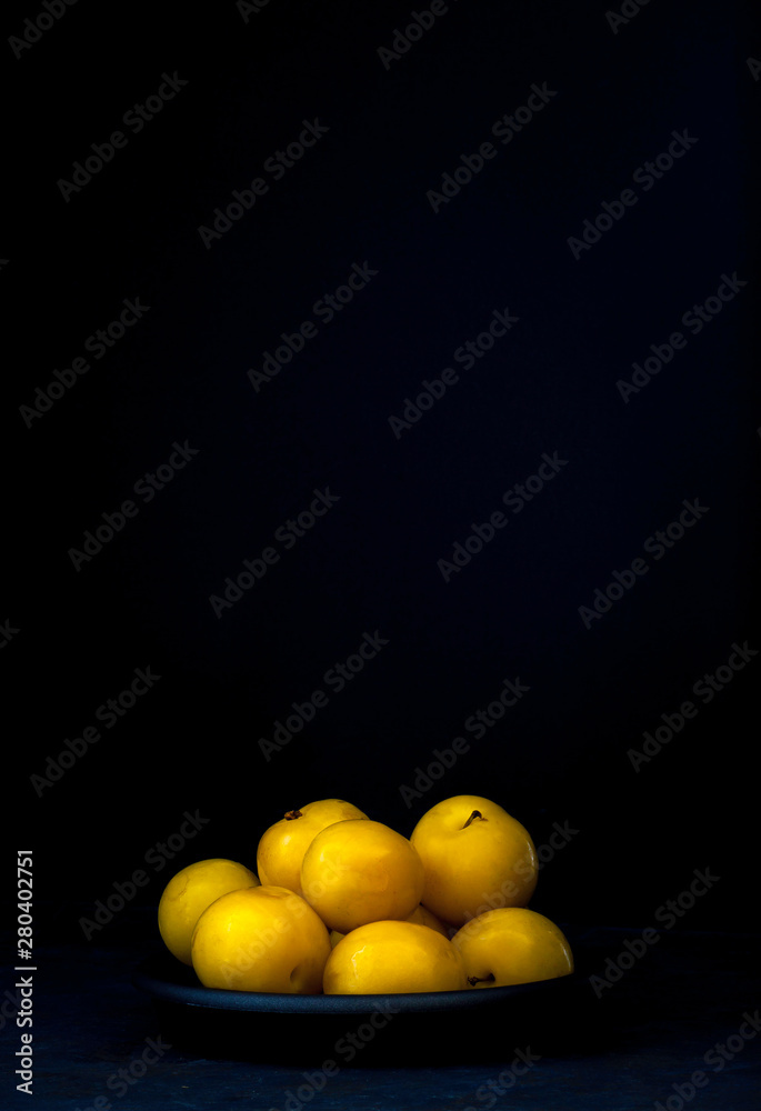 YELLOW PLUMS IN TRAY ON BLACK BACKGROUND