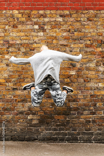 Young girl jumps in front of a brown brick wall photo