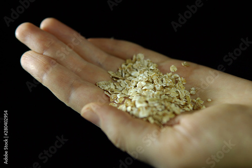 Close-up of fingers holding handful of oatmeal in hand on black background. © _vsevolod