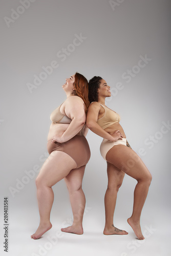 Two calm fat female friends posing for camera in studio