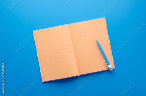 Open orange notebook with blue pens on blue background. © Moseva_Alena