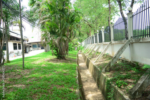 the cement vent near the metal fence with the trees ,palms and grass behind the buildings