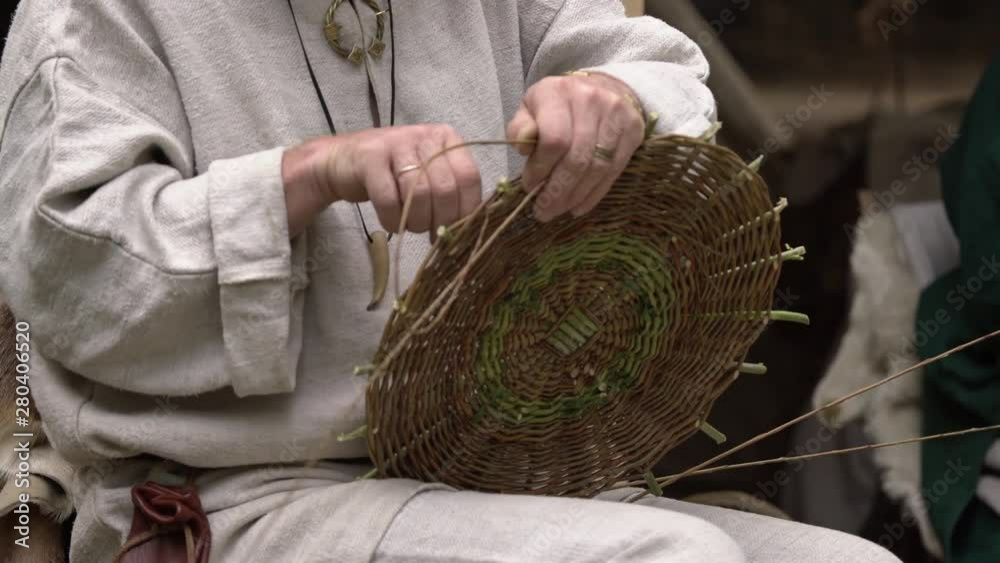 Close up of craftsman wearing rural clothes making wicker basket of twigs. Traditional handmade weaving technique at rural village