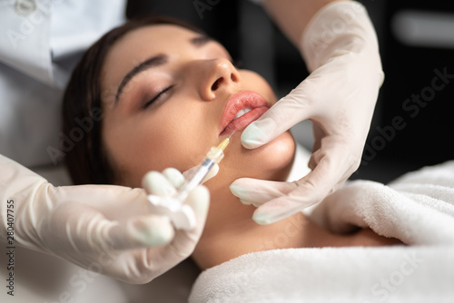 Beautician in sterile gloves making injection in woman lips