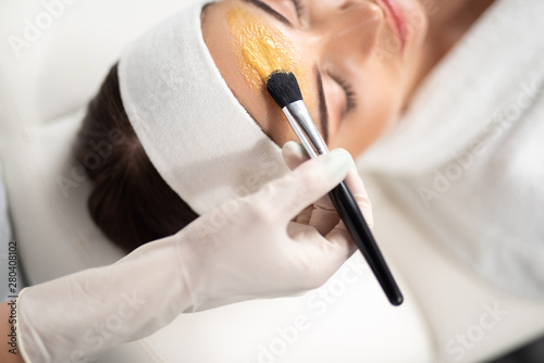 Beautician applying gold cosmetic mask on lady forehead