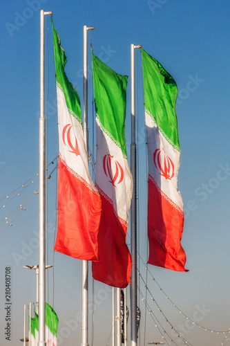 Three iranian flags on poles against a blue sky