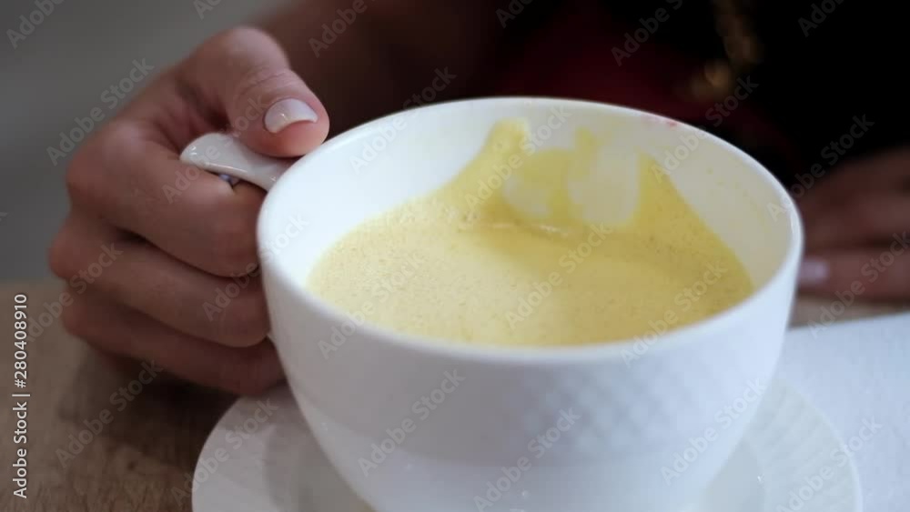 Woman hand holding and drinking cup of almond milk and tumeric curcuma Woman hand holding and drinking cup of almond milk and tumeric curcuma