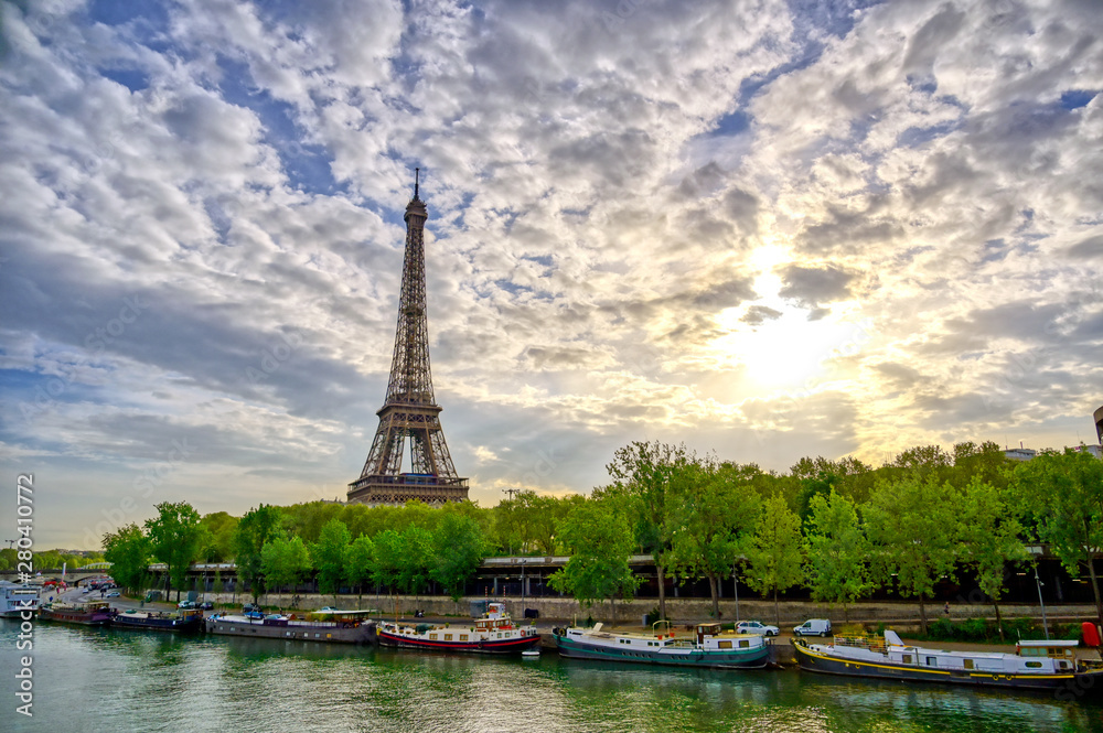 The Eiffel Tower across the Seine River in Paris, France on a sunny day with beautiful clouds.