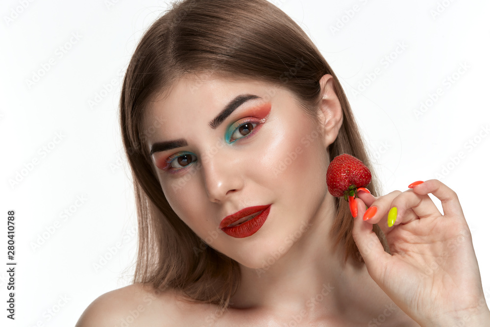 Closeup portrait of a beautiful young woman with bright color make-up holding strawberry near the face. Closeup portrait of a beautiful young woman with bright color make-up holding strawberry near the face.