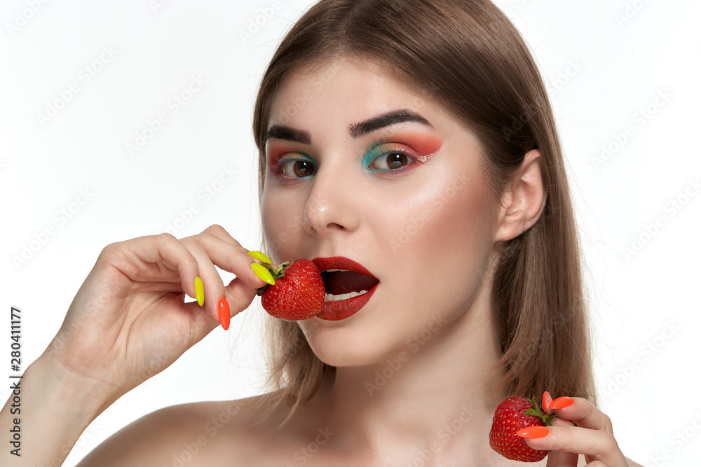 Closeup portrait of a beautiful young woman with bright color make-up holding strawberry near the face. Closeup portrait of a beautiful young woman with bright color make-up holding strawberry near the face.
