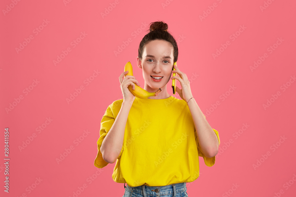 Smiling model with a hair bun in a yellow t-shirt holding banana and yellow smartphone