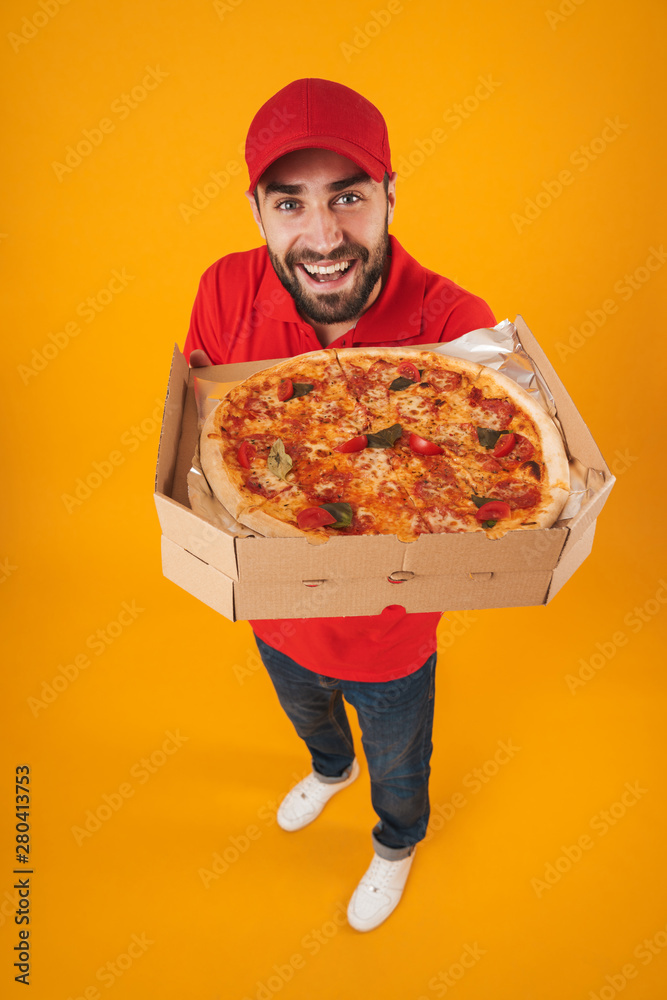 Full length image of handsome delivery man in red uniform smiling and holding pizza box Full length image of handsome delivery man in red uniform smiling and holding pizza box