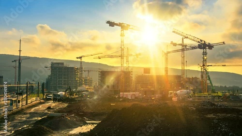 Time-lapse footage of a large construction site with several busy cranes in golden sunlight
