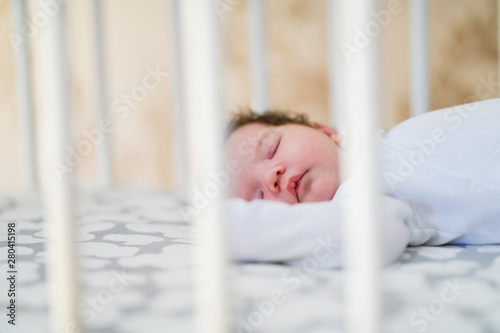The baby sleeps in the crib. A charming baby sleeps in a crib for sleeping attached to the bed of the parents. A small child having a nap in the crib. Baby in the sun nursery