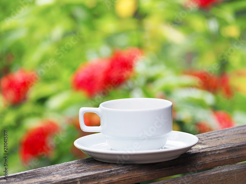 white cup of coffee over green floral abstract blur background.