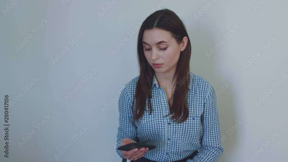 Confident girl sits and uses smartphone on background Confident girl sits and uses smartphone on background