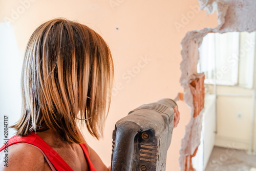 Tableau sur toile Back view of woman using pneumatic hammer drill to destroy the wall in her apart