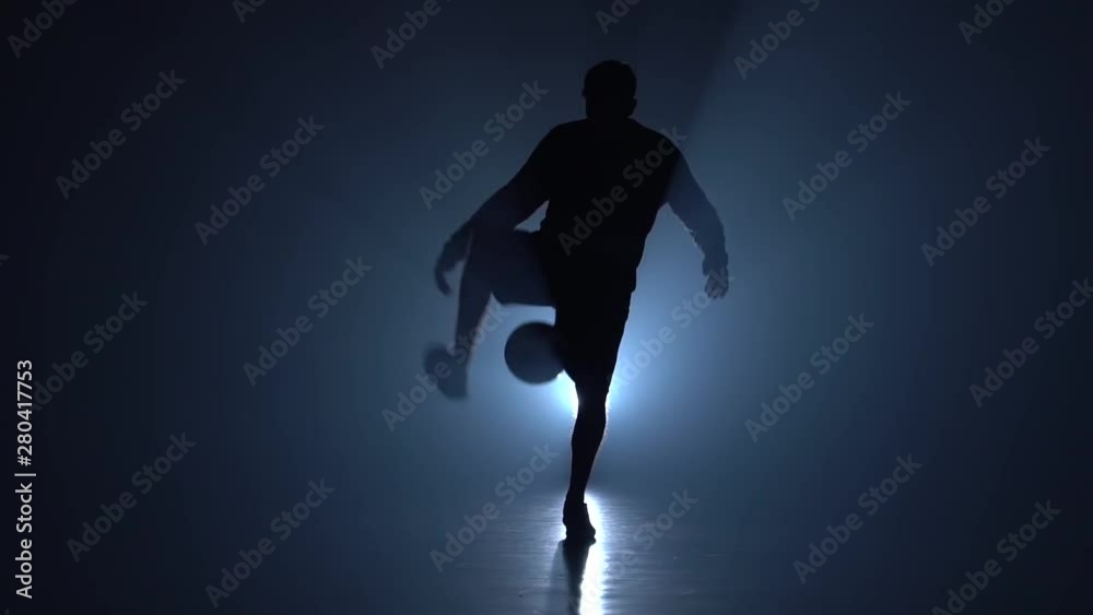 Football freestyle. Slow motion, football player stuffing ball on feet in twilight.
