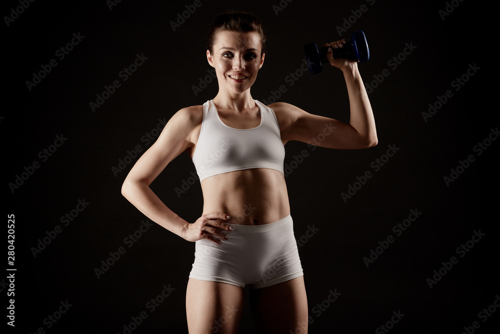 Fit woman in sportswear shows her body off and lifts a dumbbell. Fit woman in sportswear shows her body off and lifts a dumbbell.