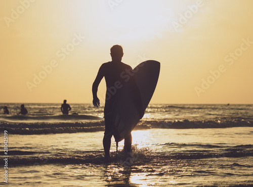 Surfer carrying the board out to sea at sunset time