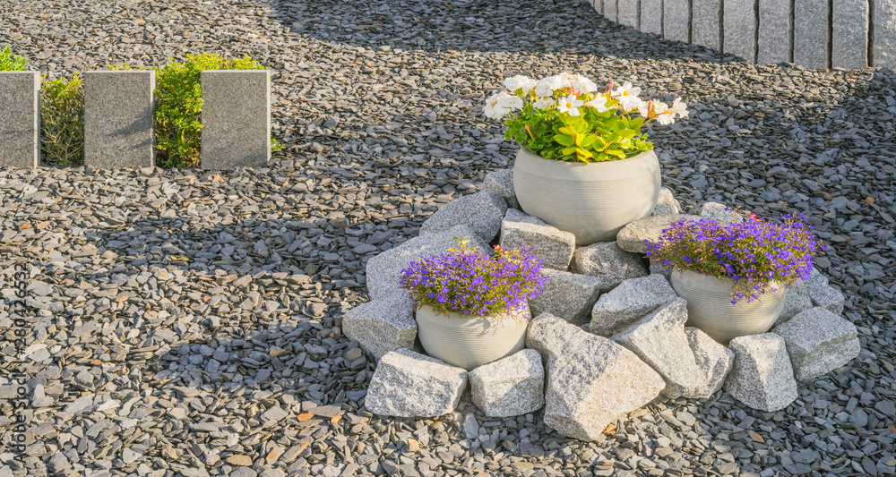 Steingarten mit Stelen aus Granit und Blumen in Blumenkübeln