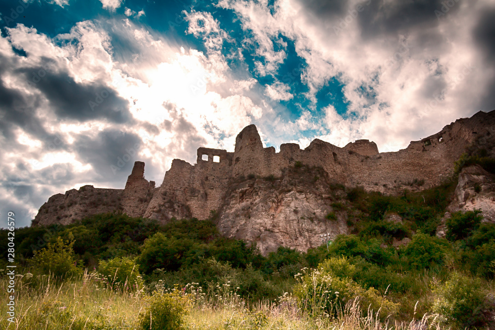 The ruins of a castle on a large hill under a cloudy sky.
