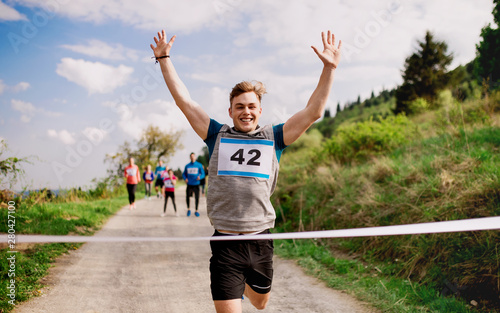 Картината върху платно Young man runner crossing finish line in a race competition in nature