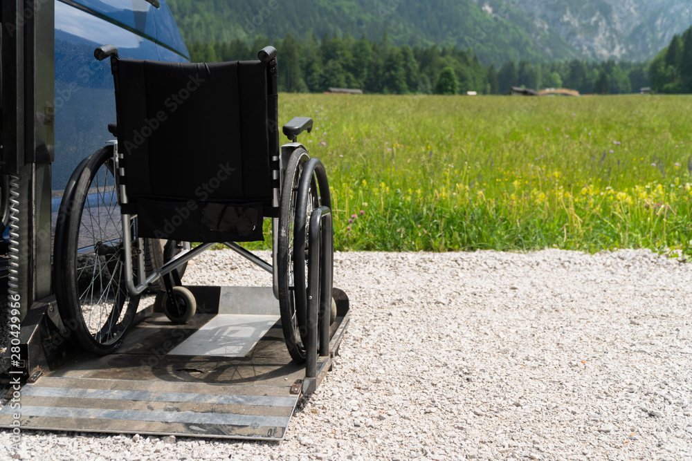 Black electric lift specialized vehicle for people with disabilities. Empty wheelchair on a ramp with nature and mountains in the back