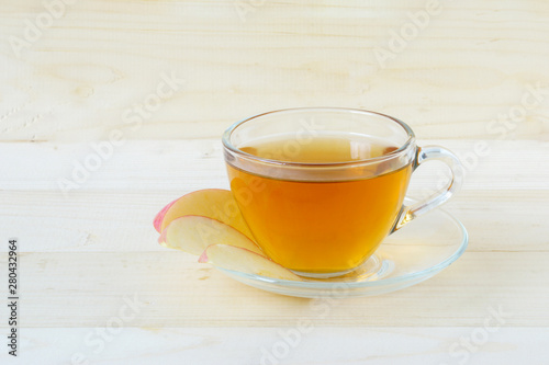Hot tea in glass and slice red apple in disk on wooden background